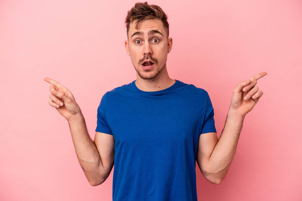 Young caucasian man isolated on pink background pointing to different copy spaces, choosing one of them, showing with finger. - Foto, immagini