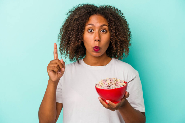 Young african american woman holding a bowl of cereals isolated on blue background having some great idea, concept of creativity. - Zdjęcie, obraz