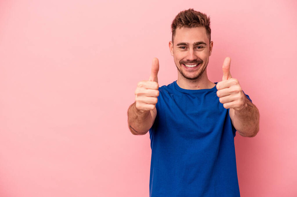 Young caucasian man isolated on pink background smiling and raising thumb up - Fotó, kép