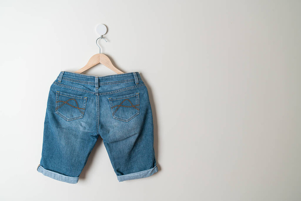 джинсы короткие, висящие на деревянной вешалке на стене - Фото, изображение