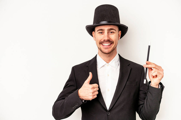 Giovane uomo mago caucasico che tiene una bacchetta isolata su sfondo bianco sorridente e sollevando il pollice verso l'alto - Foto, immagini