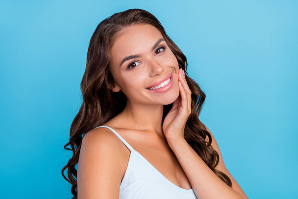Photo of tender pretty charming lady hand cheekbone shiny smile wear white top isolated blue color background - Fotoğraf, Görsel