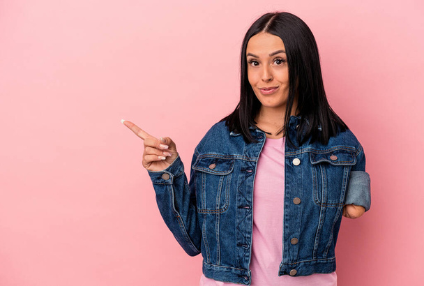 Young caucasian woman with one arm isolated on pink background smiling and pointing aside, showing something at blank space. - Photo, Image