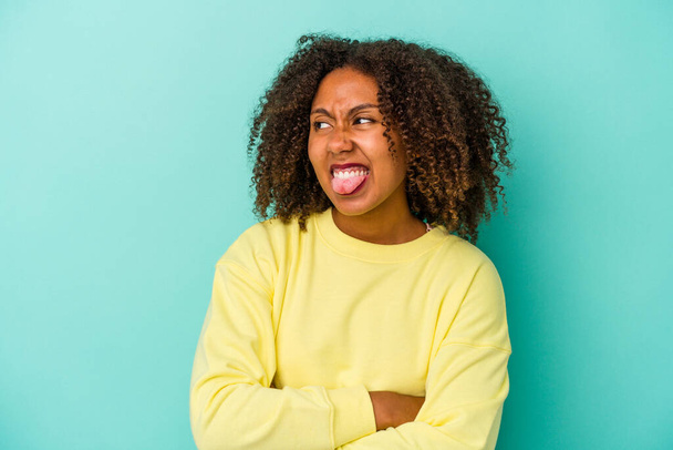 Young african american woman with curly hair isolated on blue background funny and friendly sticking out tongue. - Photo, Image
