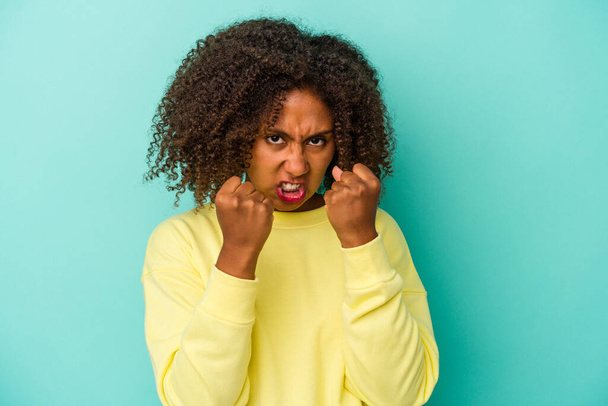 Jeune femme afro-américaine aux cheveux bouclés isolé sur fond bleu bouleversé crier avec les mains tendues. - Photo, image