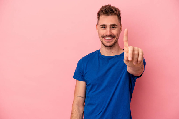 Giovane uomo caucasico isolato su sfondo rosa mostrando il numero uno con il dito. - Foto, immagini