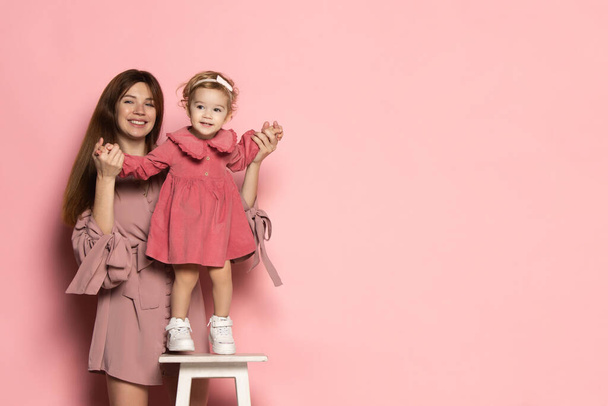 Emotional woman and little girl, caring mother and daughter isolated on pink studio background. Mothers Day celebration. Concept of family, childhood, motherhood - Photo, image