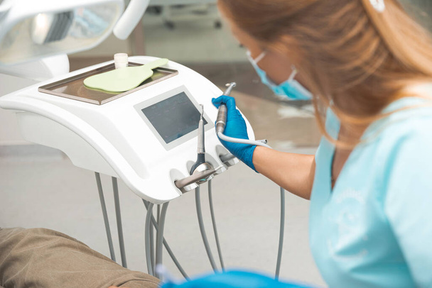 Mladá zubařka v uniformě je v pracovním procesu se zubními nástroji v blízkosti židle.  - Fotografie, Obrázek