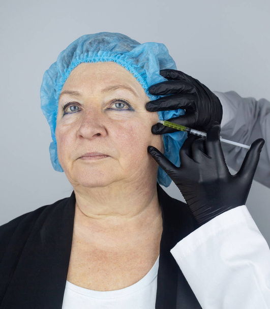 Wstrzyknięcie toksyny botulinowej. Starsza kobieta na spotkaniu z kosmetyczką, która przygotowuje się do wykonania zastrzyków przeciwzmarszczkowych. Luźna skóra i niedociśnienie. Mimiczne zmarszczki i konturowanie - Zdjęcie, obraz