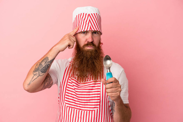 Young caucasian ginger man with long beard holding a scoop isolated on pink background pointing temple with finger, thinking, focused on a task. - Foto, Bild
