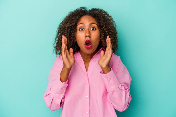 Junge afrikanisch-amerikanische Frau mit lockigem Haar isoliert auf blauem Hintergrund überrascht und schockiert. - Foto, Bild