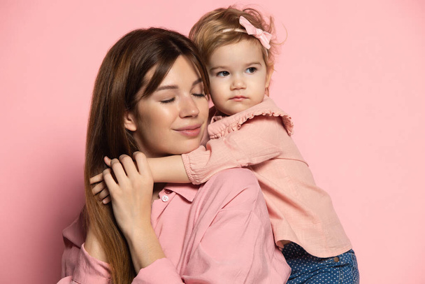Happy woman and little girl, caring mother and daughter isolated on pink studio background. Mothers Day celebration. Concept of family, childhood, motherhood - Photo, Image