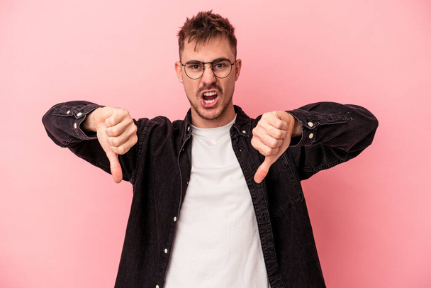 Young caucasian man isolated on pink background showing thumb down and expressing dislike. - Photo, Image