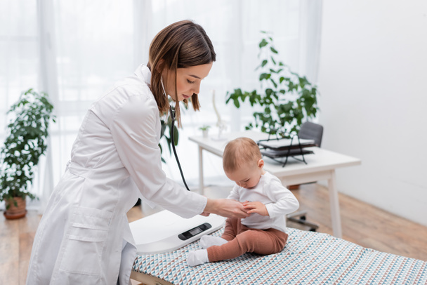 Brünette Ärztin untersucht Baby mit Stethoskop im Krankenhaus  - Foto, Bild