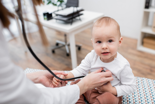 Médecin de famille flou examinant un enfant avec stéthoscope en clinique  - Photo, image