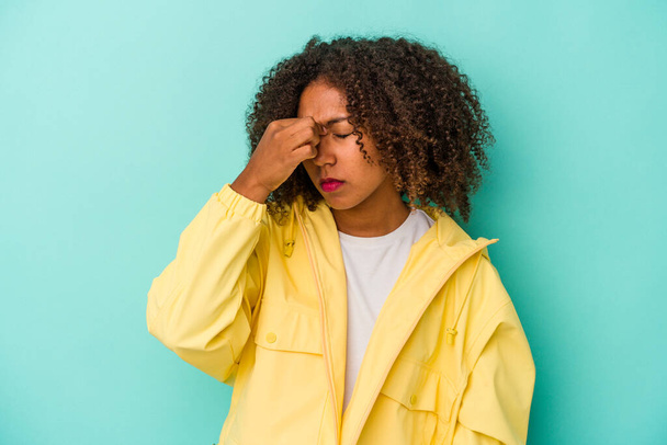 Giovane donna afroamericana con i capelli ricci isolati su sfondo blu con mal di testa, toccando la parte anteriore del viso. - Foto, immagini