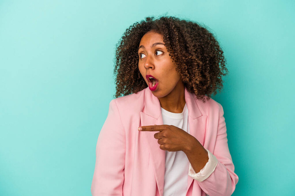 Young african american woman with curly hair isolated on blue background points with thumb finger away, laughing and carefree. - Foto, immagini
