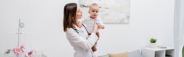 Joven médico de familia en cuna blanca sosteniendo al bebé en casa, pancarta  - Foto, imagen