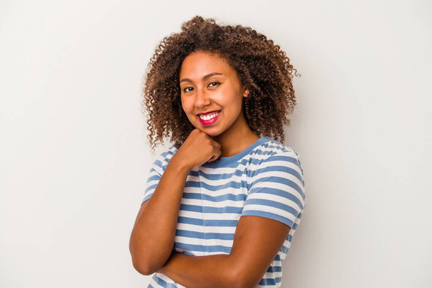 Молода афроамериканська жінка з кучерявим волоссям на білому фоні посміхається щаслива і впевнена, торкаючись підборіддя рукою.. - Фото, зображення