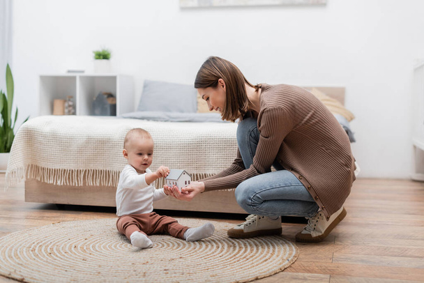 Genitore positivo che tiene la casa giocattolo vicino al figlio sul tappeto in camera da letto  - Foto, immagini