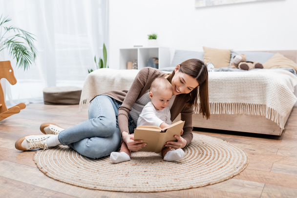 Usmívající se rodič čtení knihy poblíž chlapeček na koberec doma  - Fotografie, Obrázek