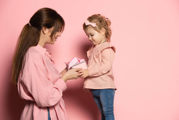 Delighted young woman and toddler, caring mother and daughter isolated on pink studio background. Mothers Day celebration. Concept of family, childhood, motherhood - Photo, image