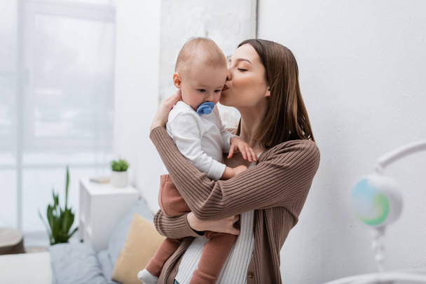 Fiatal anya csók baba fiú cumi a hálószobában  - Fotó, kép