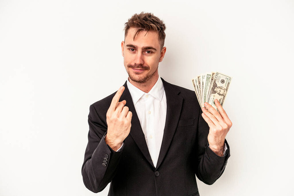 Молодий кавказький бізнесмен тримає банкноти ізольовані на білому тлі, вказуючи пальцем на вас, ніби запрошений наближається
. - Фото, зображення