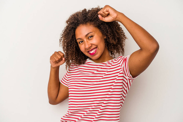 Молодая африканская американка с вьющимися волосами изолирована на белом фоне, празднуя особый день, прыгает и поднимает руки с энергией. - Фото, изображение