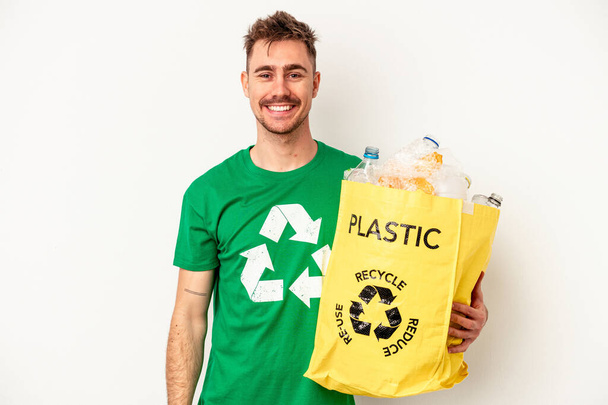 Joven hombre caucásico reciclado de plástico aislado sobre fondo blanco feliz, sonriente y alegre. - Foto, imagen