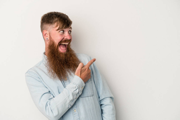 Giovane uomo zenzero caucasico con lunga barba isolata su sfondo bianco guarda da parte sorridente, allegro e piacevole. - Foto, immagini
