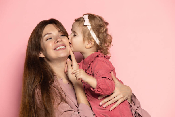 Delighted young woman and toddler, caring mother and daughter isolated on pink studio background. Mothers Day celebration. Concept of family, childhood, motherhood - Zdjęcie, obraz