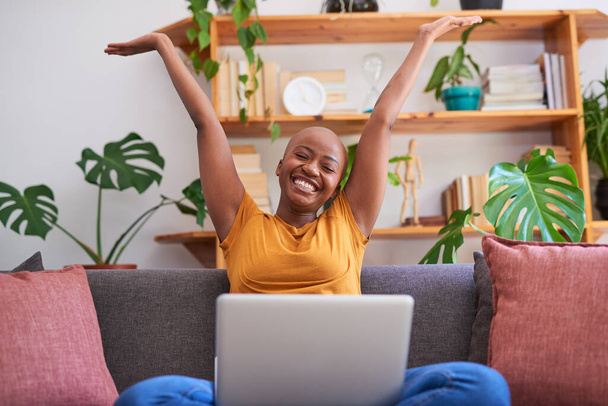 Genç bir kadın kollarını kanepede dizüstü bilgisayarla kaldırarak büyük bir zaferi kutluyor. - Fotoğraf, Görsel