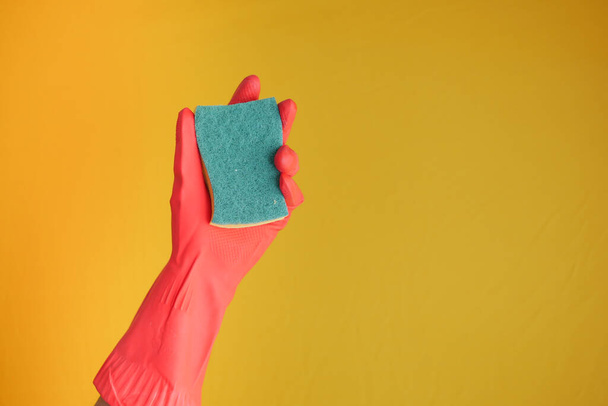  ręka w gumowych rękawiczkach trzymających gąbkę przeciwko żółtemu  - Zdjęcie, obraz