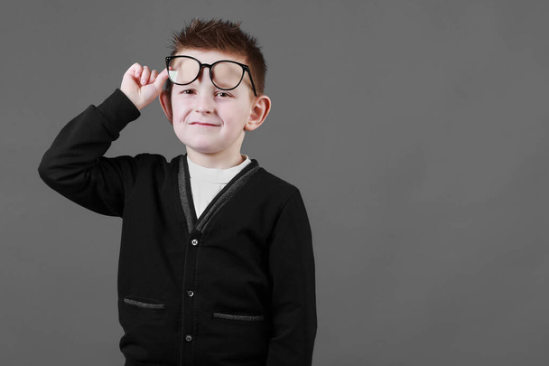 Smart child boy adjusts his glasses and having fun on the grey background, close-up. Studio juvenile portrait in casual clothes. copy space. - Fotoğraf, Görsel