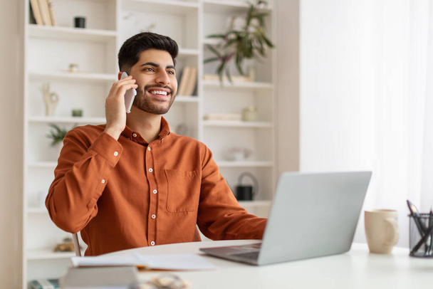 Sonriente hombre barbudo trabajando y hablando por teléfono en casa - Foto, Imagen