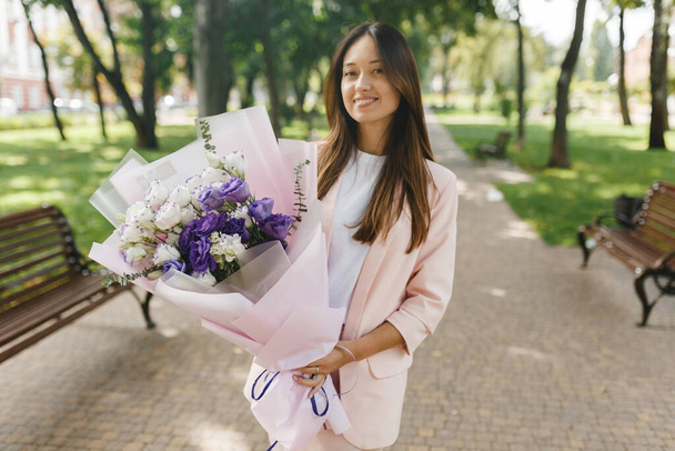 Young woman holding a blooming bouquet of fresh, roses, eustoma, eucalyptus flowers in the park - Zdjęcie, obraz