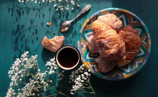 Good morning! Black coffee and croissants on a table. Sunny picture with pastries and flowers. Food still life photo.  - Photo, Image