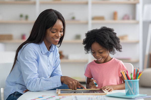 Весела афроамериканська жінка-терапевт викладає абетку маленької дівчинки
 - Фото, зображення