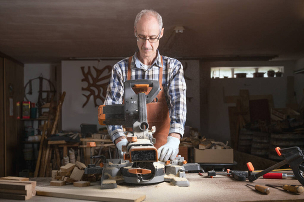 Ξυλουργός πριονίζει μια ξύλινη σανίδα με ηλεκτρικό δισκοπρίονο μηχάνημα σε εργαστήριο ξυλουργικής. Έννοια DIY ξύλου εργασίας - Φωτογραφία, εικόνα