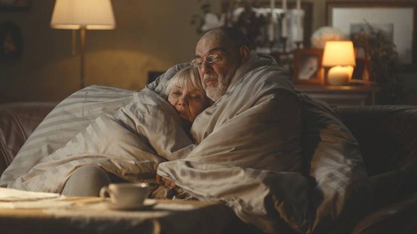 Λυπημένο ηλικιωμένο ζευγάρι αγκαλιάζεται κάτω από κουβέρτα και μιλάει - Φωτογραφία, εικόνα