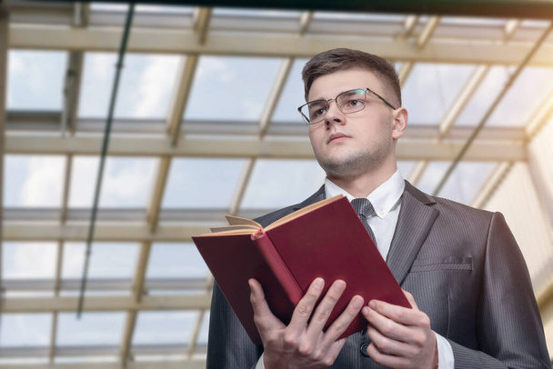 Business man in glasses and a textbook in his hands against the background of a glass roof. - Foto, afbeelding
