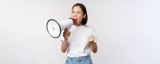 Mujer asiática segura gritando en megáfono, gritando y protestando. Chica activista usando altavoz para hablar más alto, de pie sobre fondo blanco - Foto, Imagen