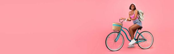 Mujer negra en ropa de verano casual montar en bicicleta sobre rosa - Foto, imagen