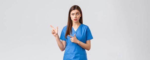 Pracownicy służby zdrowia, zapobiegać wirusom, ubezpieczenia i koncepcji medycyny. Sceptyczna i niepewna pielęgniarka lub lekarz w niebieskim fartuchu, wzbudzający podejrzenia brwi, wskazując palcami w lewo na baner - Zdjęcie, obraz