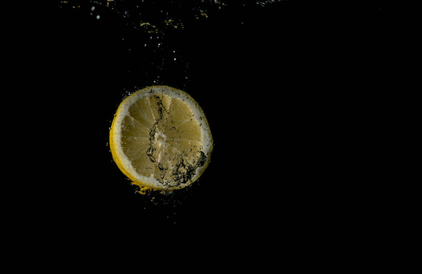 lemon falling into water on black background - Фото, изображение