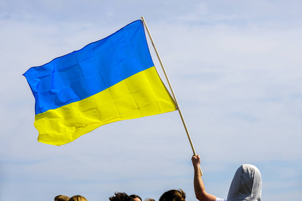 a flagpole with the flag of Ukraine in a raised hand over people's heads against a background of blue sky - Photo, Image