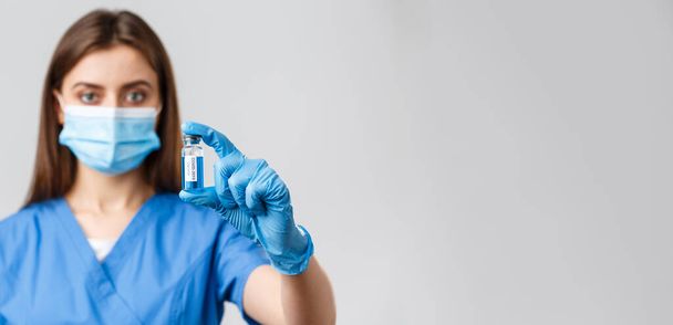 Covid-19, preventing virus, health, healthcare workers and quarantine concept. Close-up of serious-looking young doctor or nurse in clinic, lab showing coronavirus vaccine in ampoule - Фото, изображение