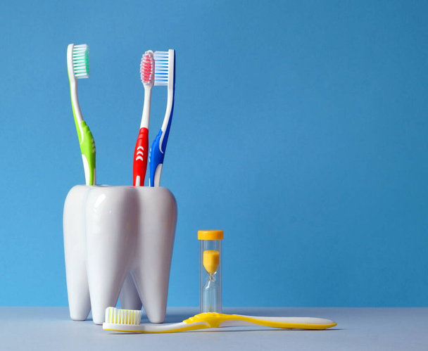 Tandenborstels zitten in een glas, er is een zandloper naast, om de tijd van het tandenpoetsen te tellen, en een borstel ligt op de tafel - Foto, afbeelding