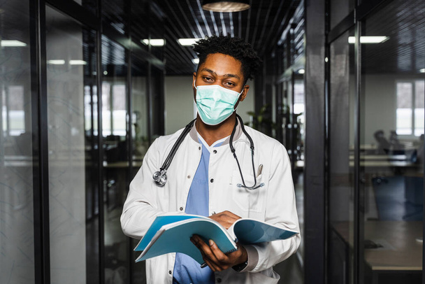 African doctor in mask with books in medical clinic. Black medical student study in university - Photo, Image